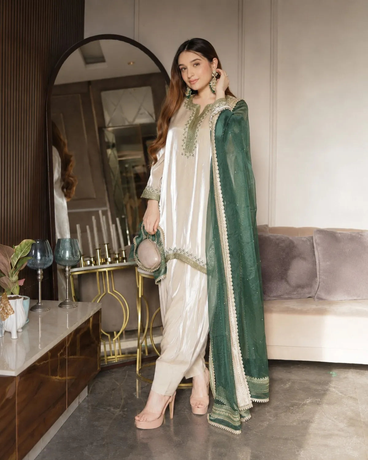Woman in a green and white traditional outfit standing in a modern living room.