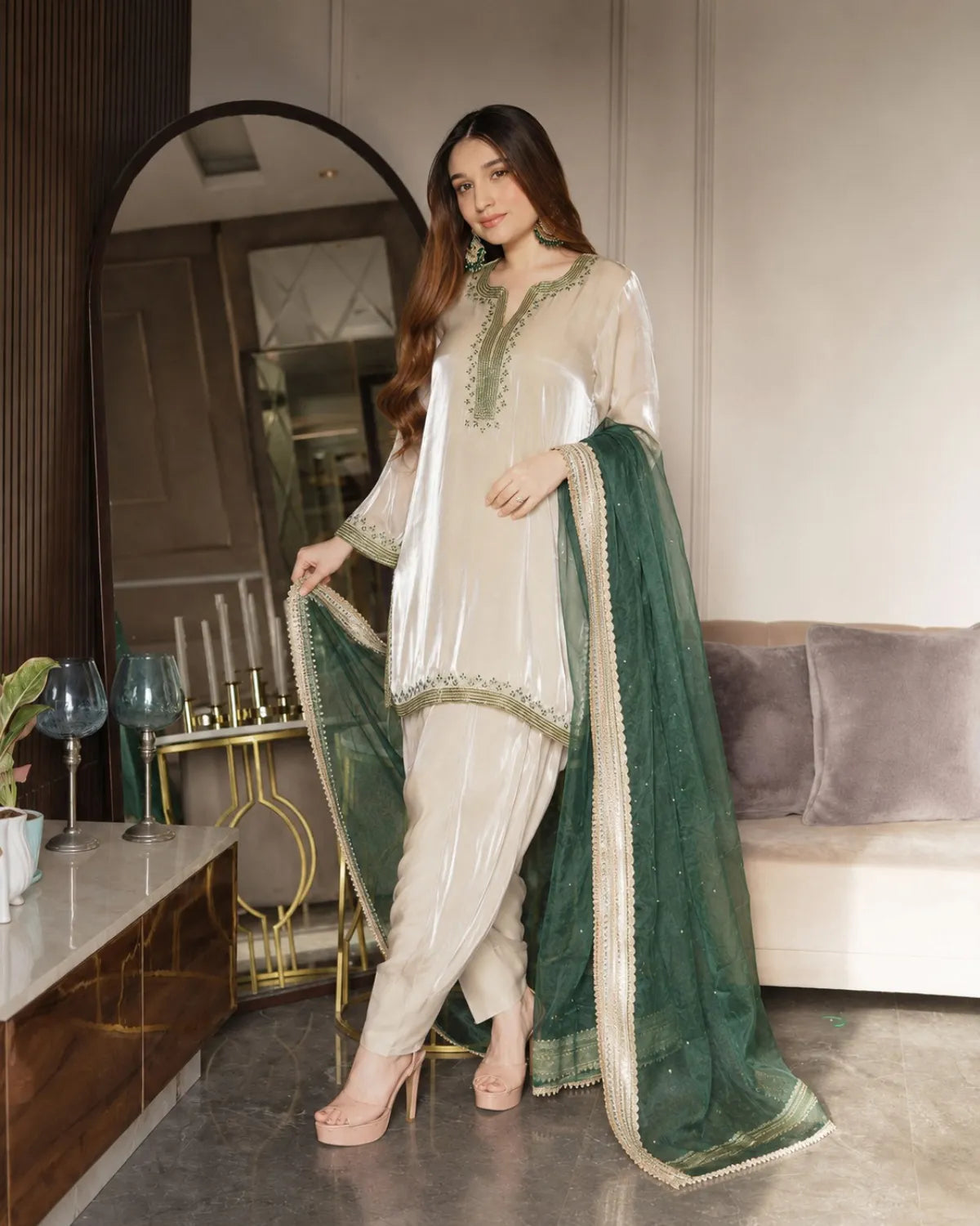 Woman in a traditional outfit with a green dupatta in a modern living room.