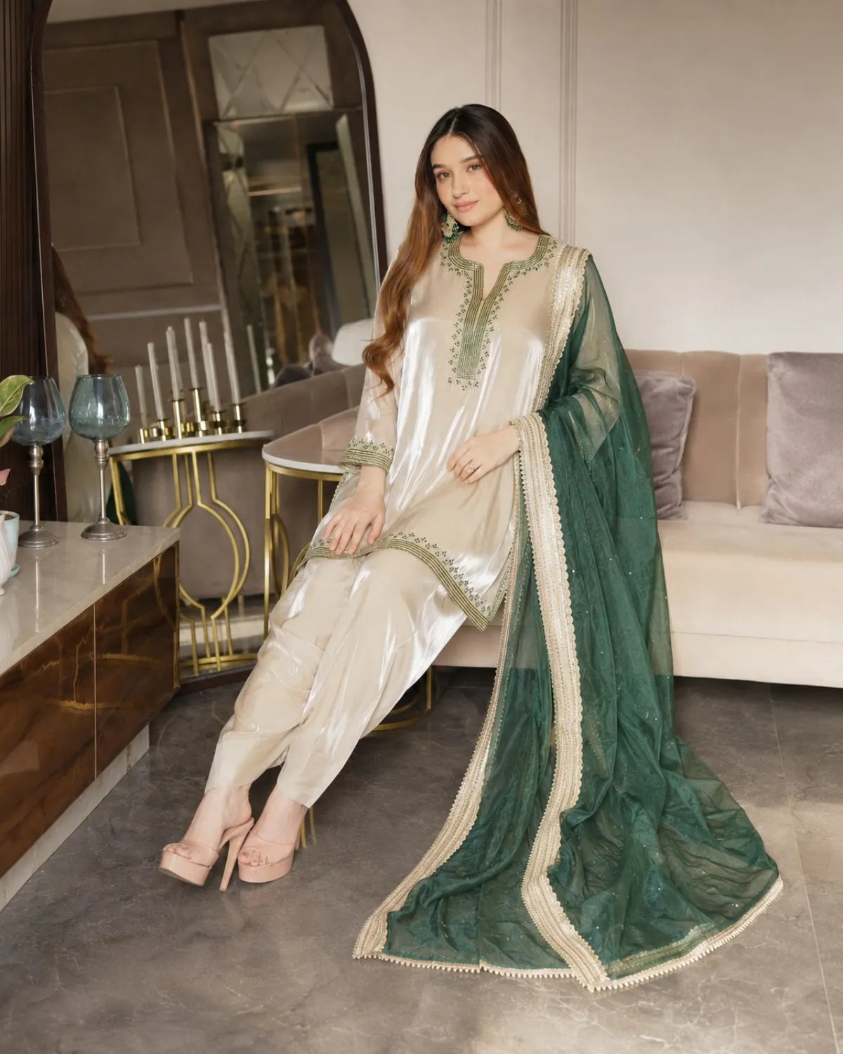 Woman in a green and white traditional outfit sitting in a modern living room.