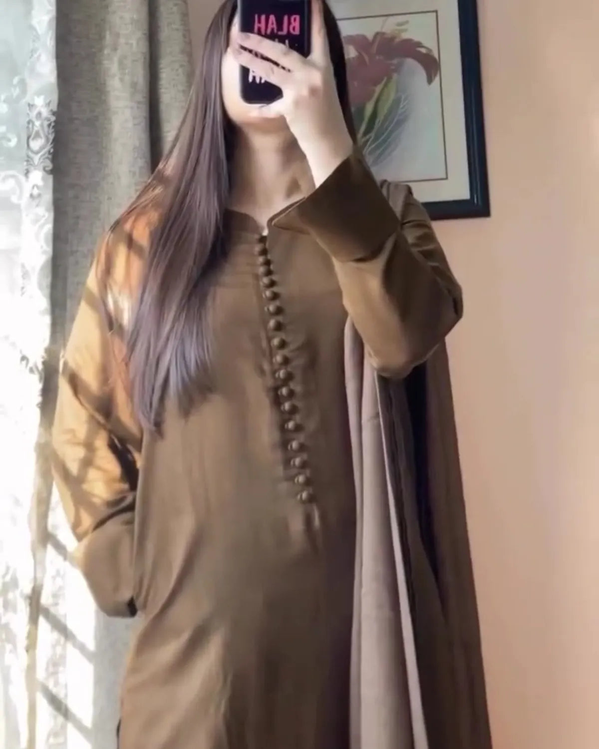 Person wearing a brown outfit with a long scarf, taking a mirror selfie.