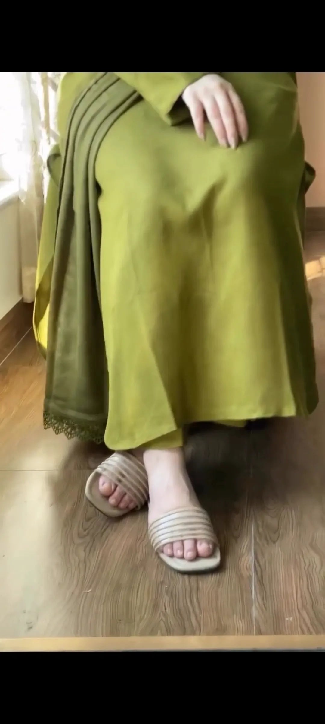 Person wearing a green outfit with a patterned scarf on a wooden floor.