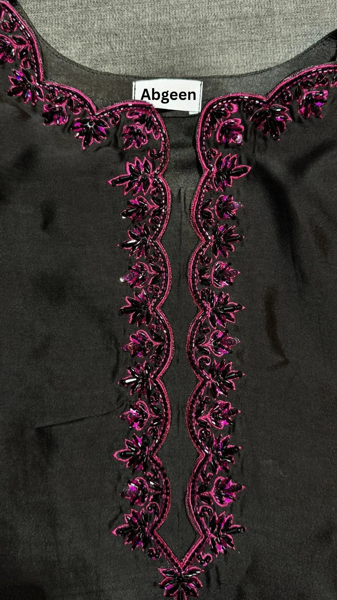 Black garment with pink embroidery and 'Abgeen' label on a gray background