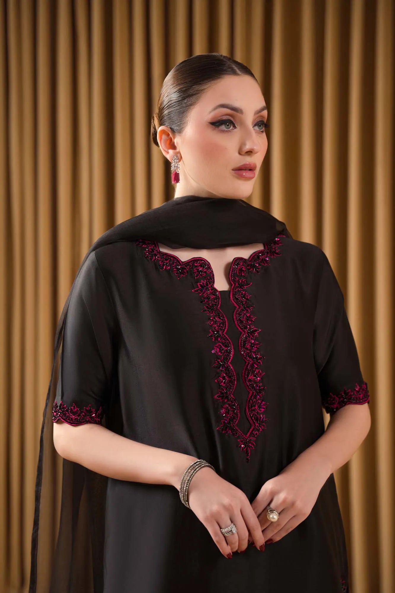 Woman wearing a black outfit with red embroidery against a brown curtain background