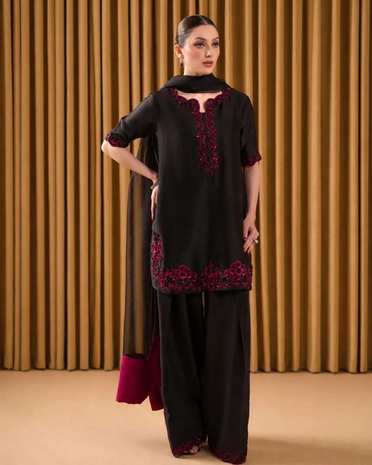 Woman wearing a black outfit with red embroidery against a brown curtain background