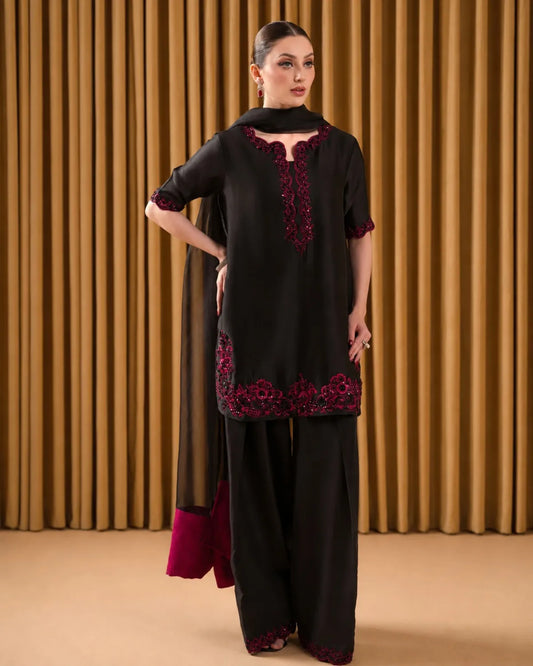 Woman wearing a black outfit with red embroidery against a brown curtain background