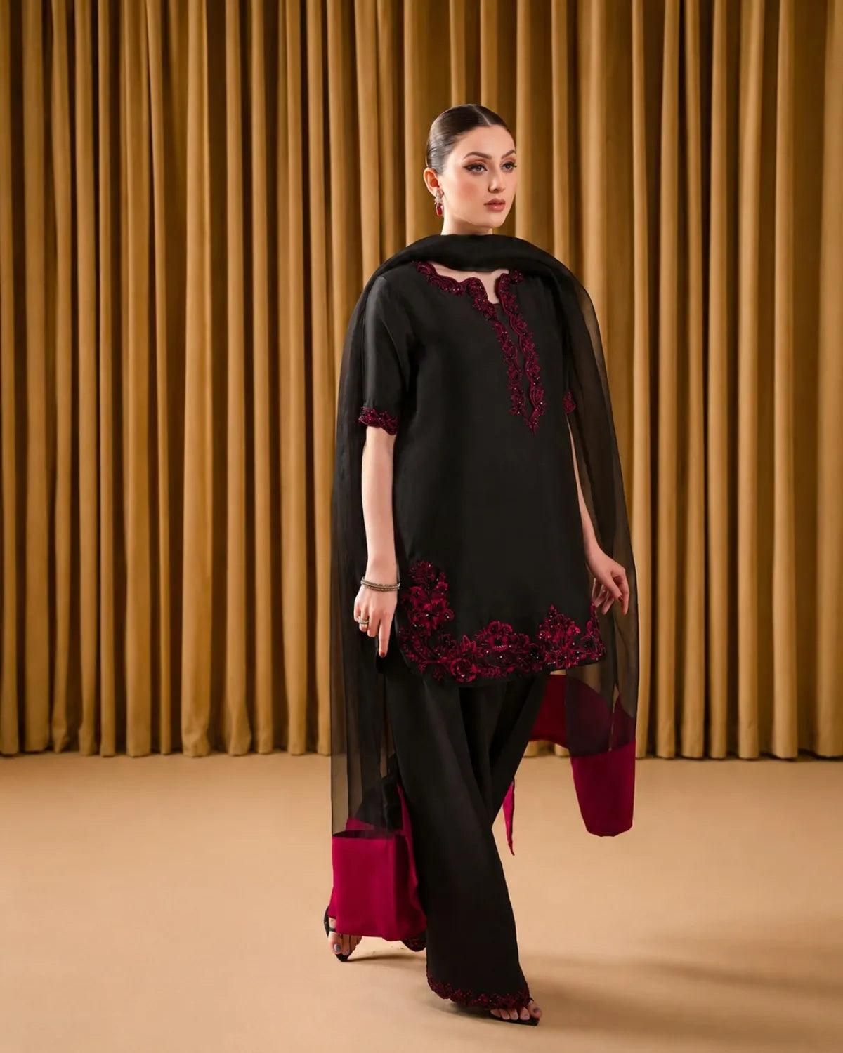 Woman wearing a black and red embroidered outfit against a gold curtain background