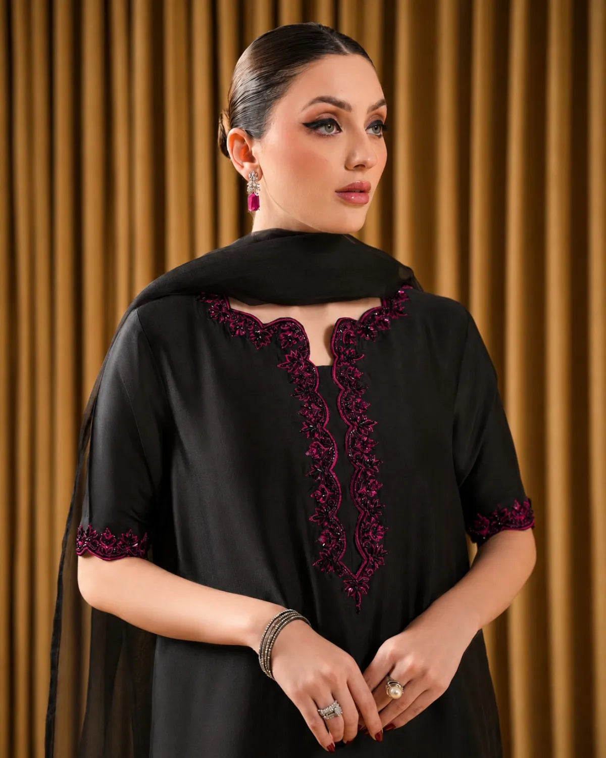 Woman wearing a black outfit with intricate purple detailing against a brown curtain background