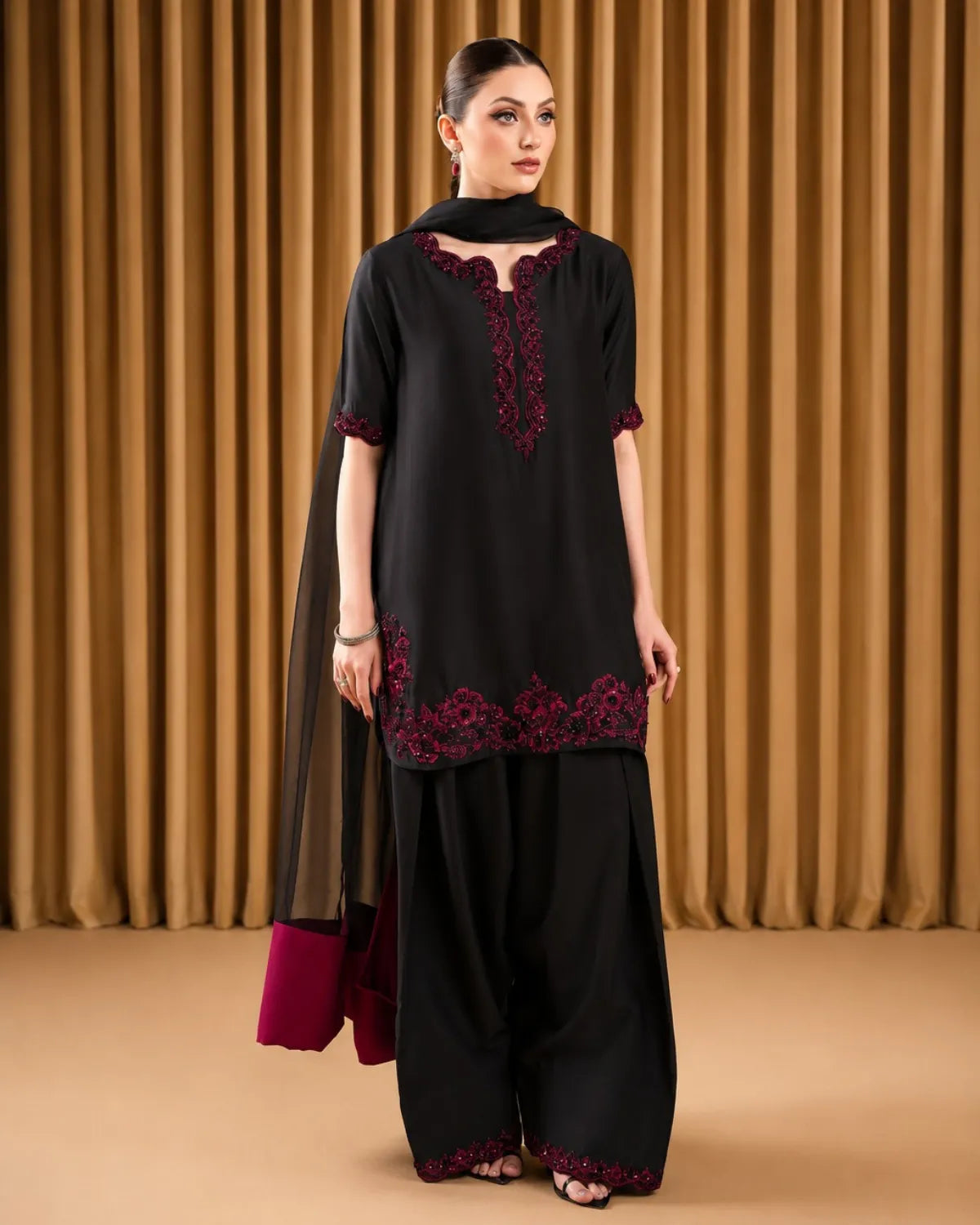 Woman wearing a black outfit with red embroidery against a brown curtain background