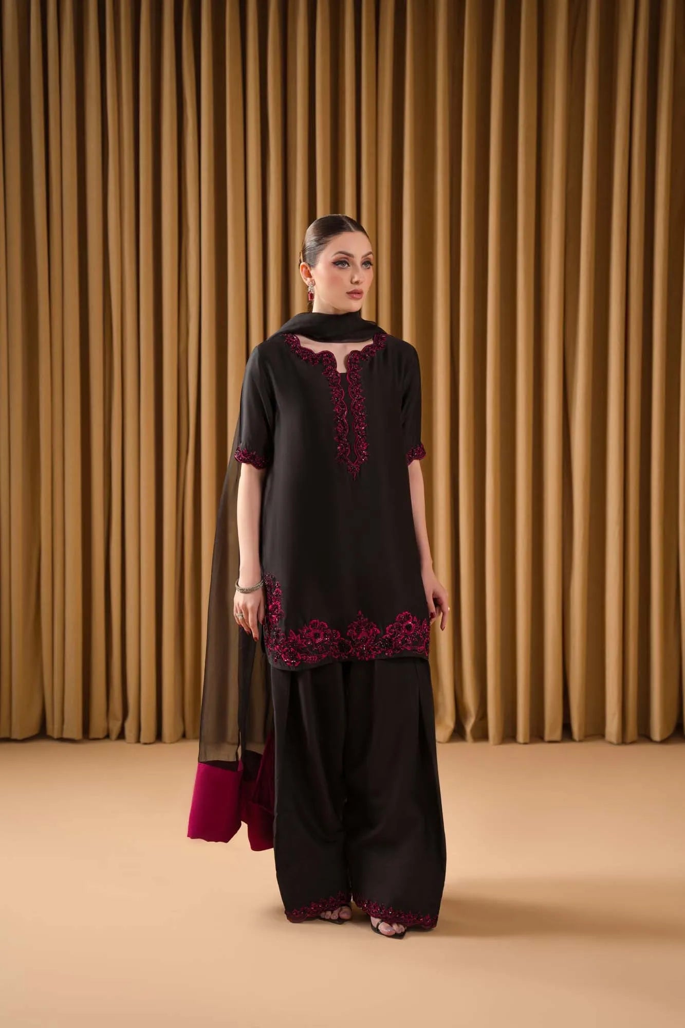 Woman wearing a black and red embroidered outfit against a beige curtain background