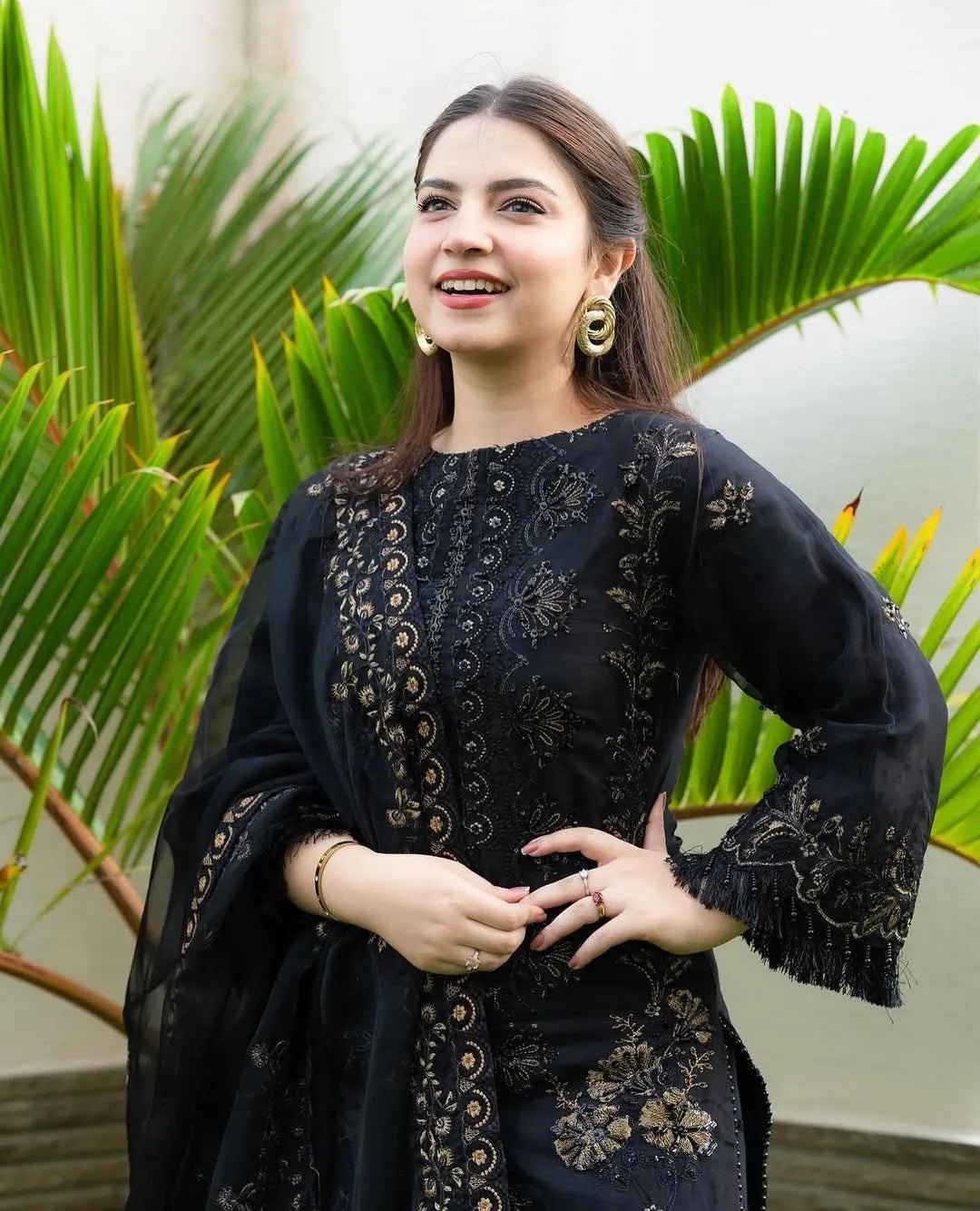 Woman wearing a black embroidered dress with green plants in the background
