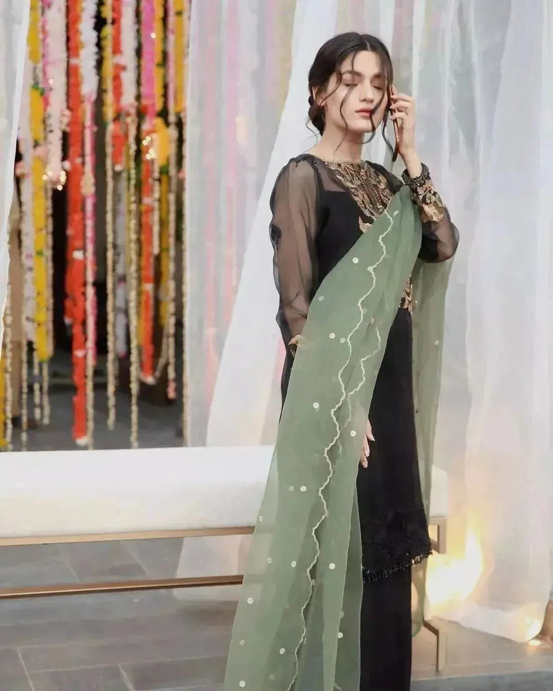 Woman holding a green saree with a blurred decorative background