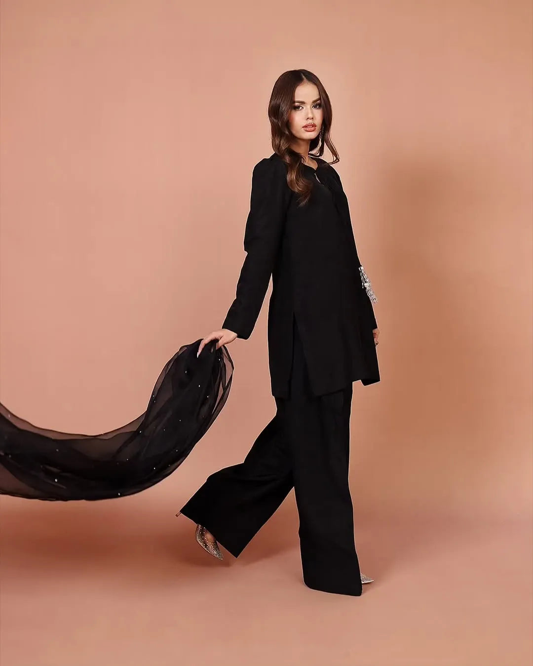 Woman in a black outfit holding a black scarf against a beige background