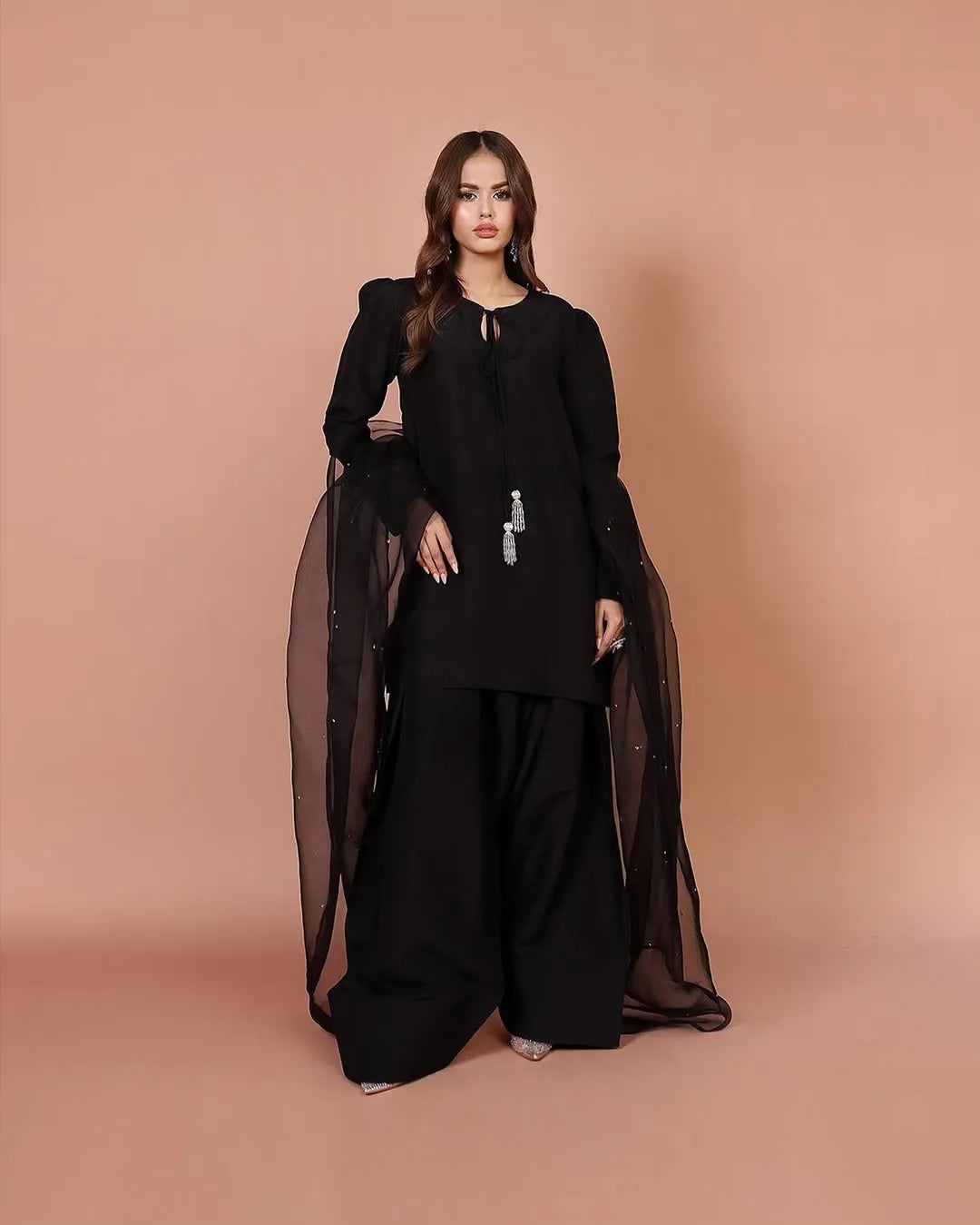 Woman wearing a black outfit with sheer sleeves against a beige background