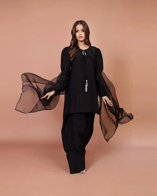 Woman wearing a black outfit with a sheer scarf against a beige background