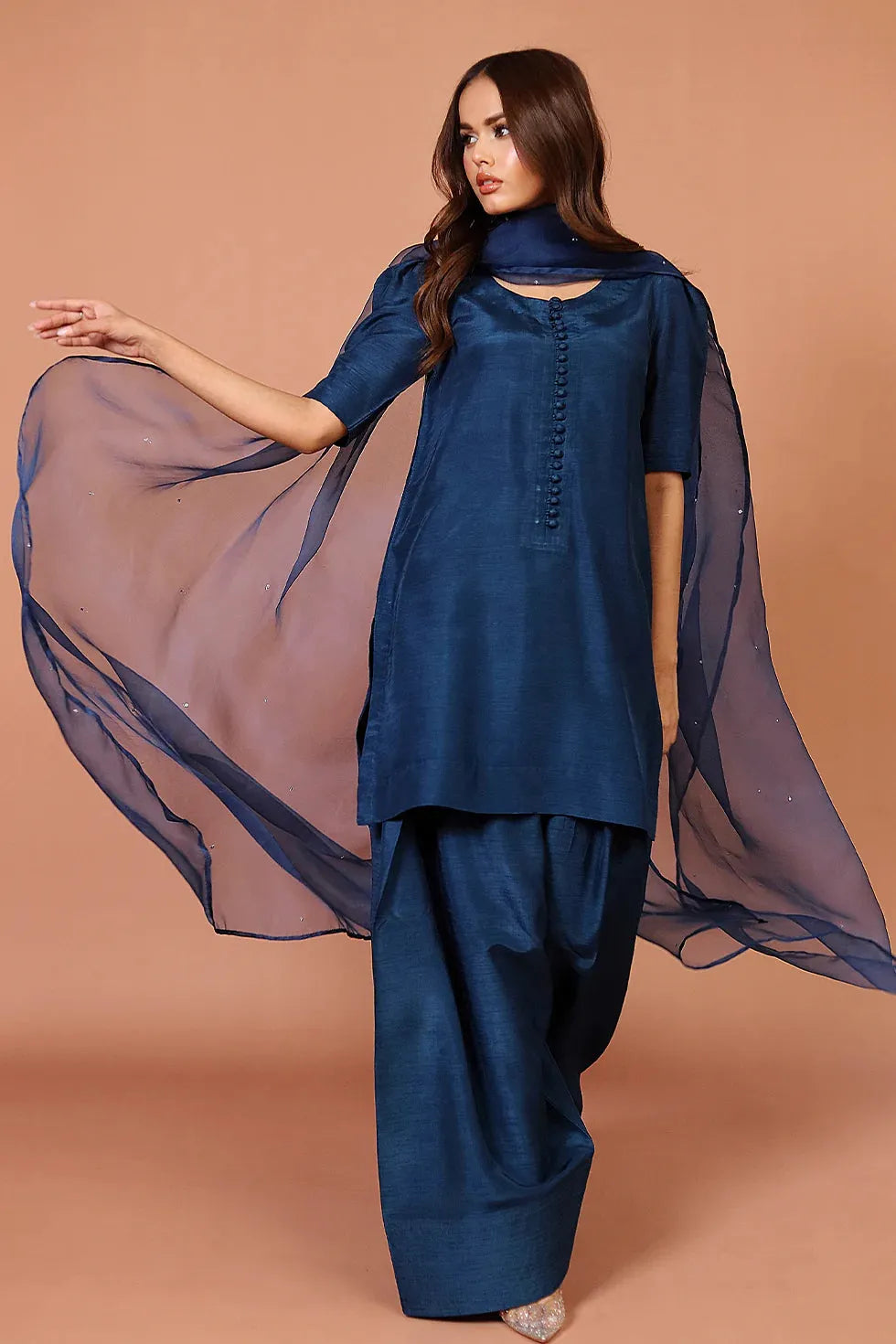 Woman wearing a blue traditional outfit with a sheer dupatta against a beige background