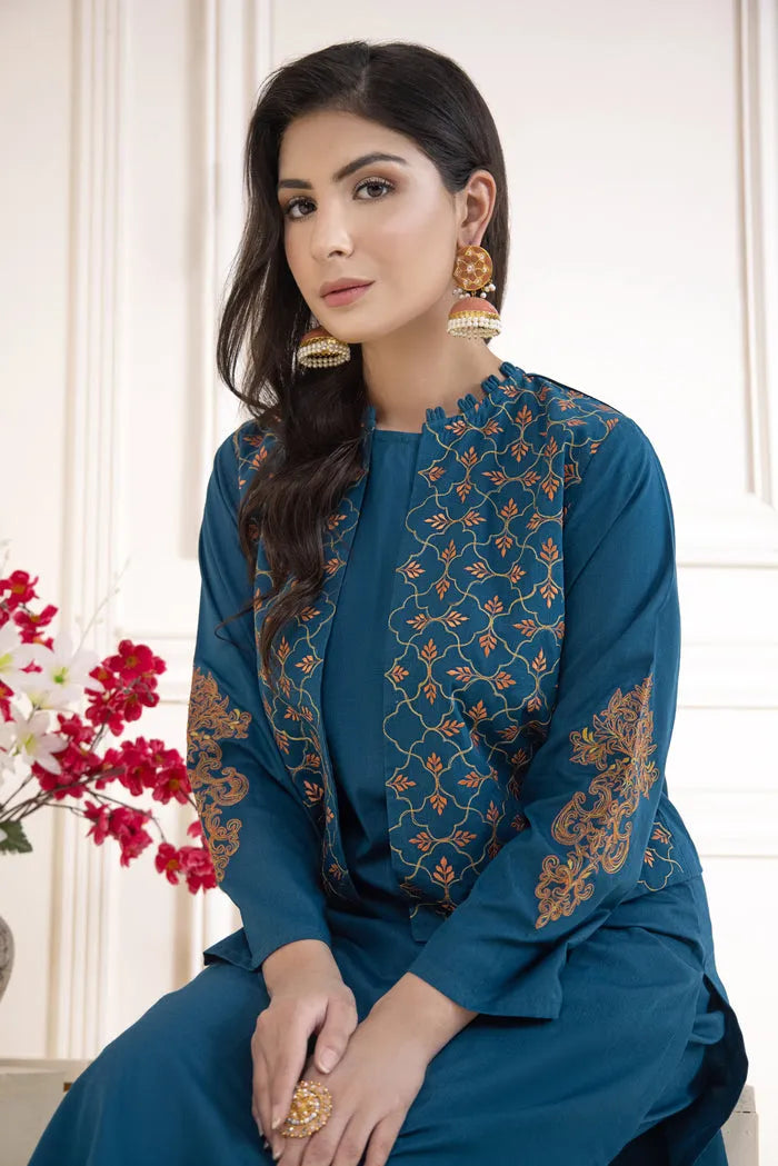 Woman wearing a blue embroidered outfit with gold details, sitting indoors.