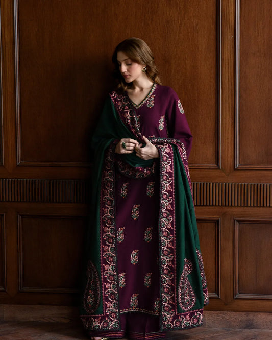 Woman wearing a long, dark purple and green embroidered dress against a wooden paneled wall.