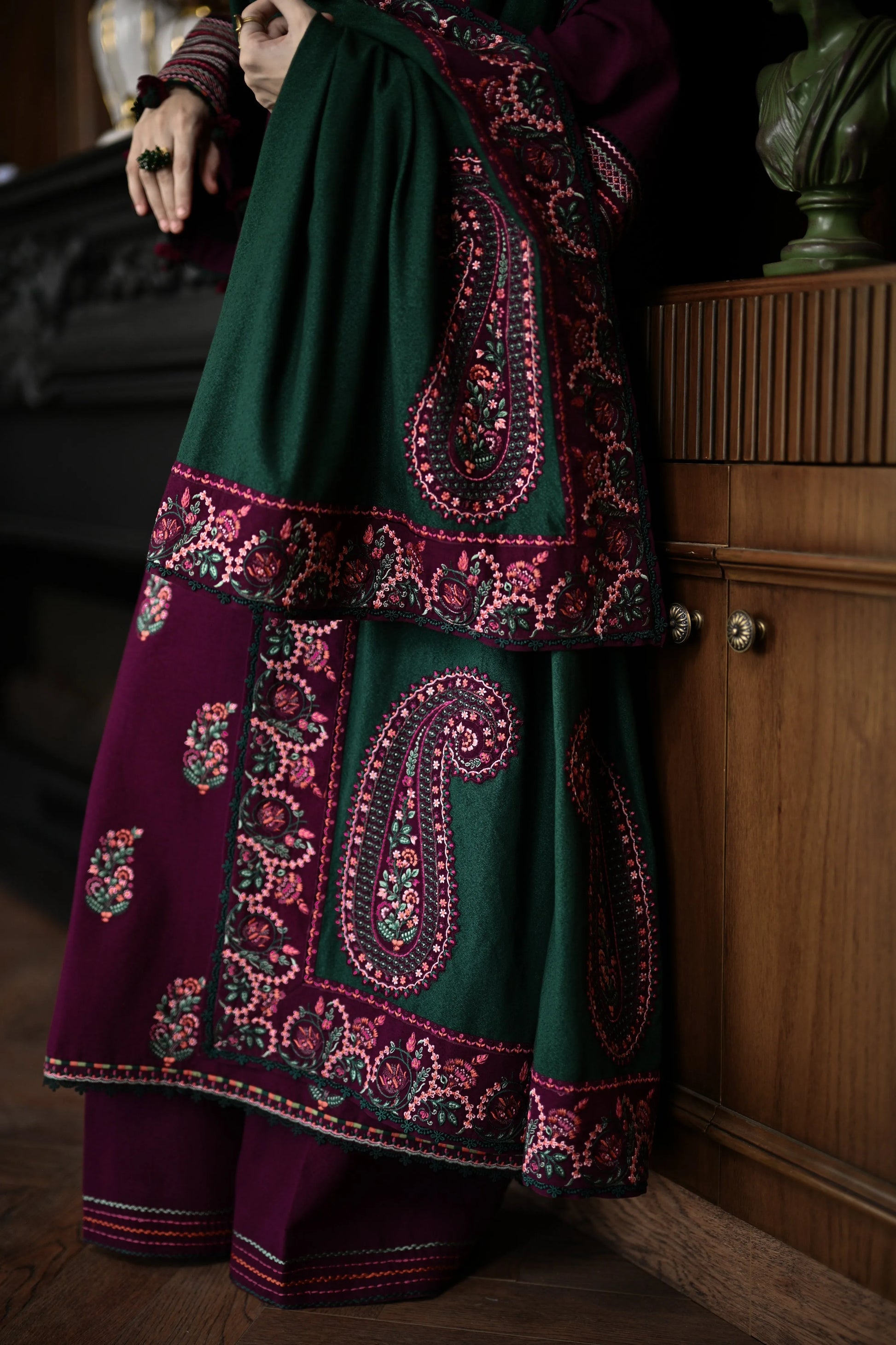 Person wearing a traditional embroidered outfit with green and purple patterns in a dimly lit room.