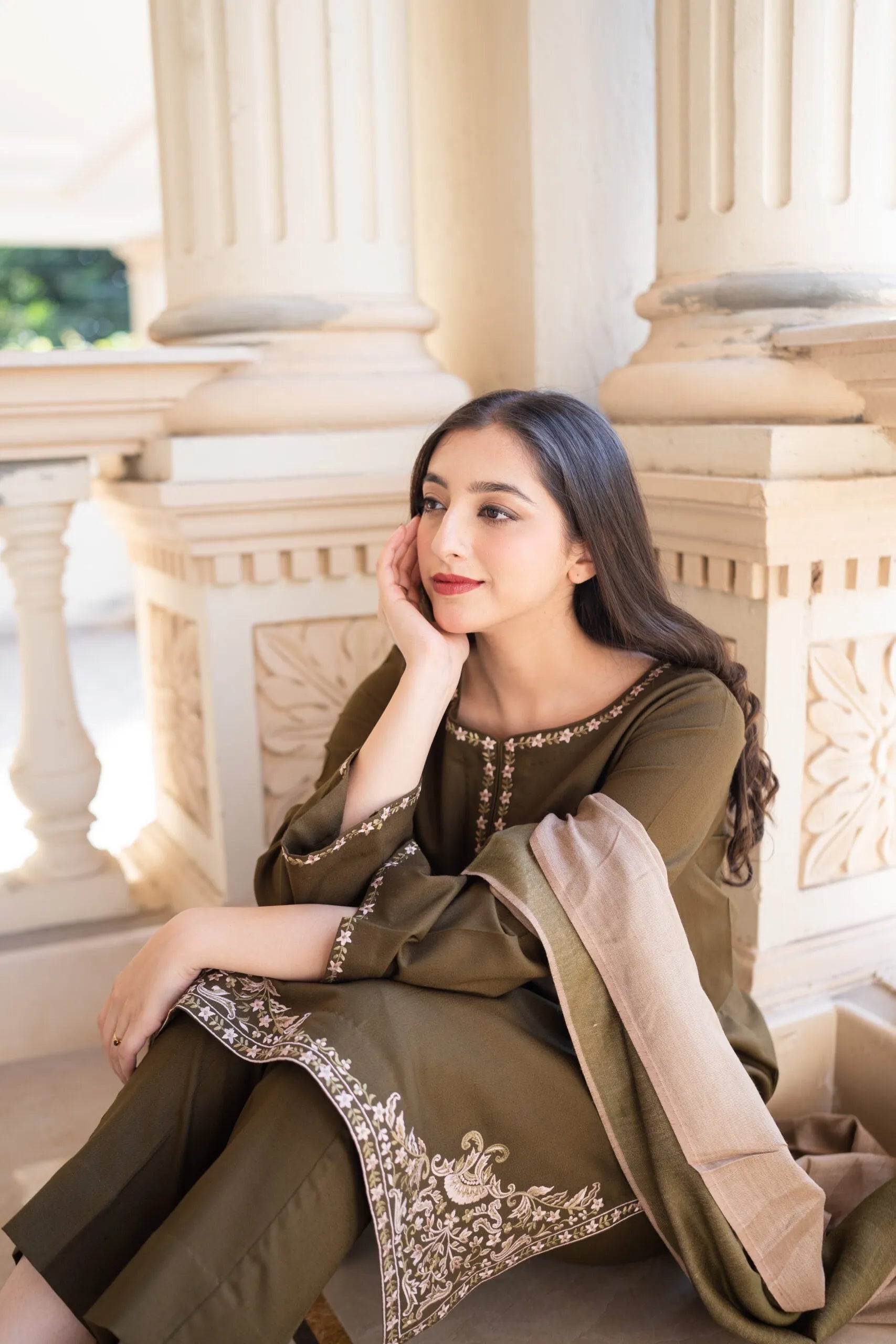Woman in traditional outfit sitting on a stone bench with classical architecture in the background