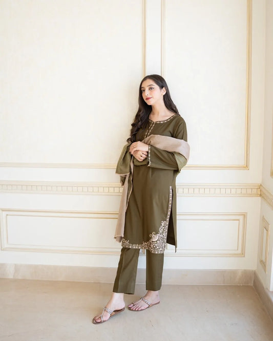 Woman in an olive green traditional outfit standing against a white wall.