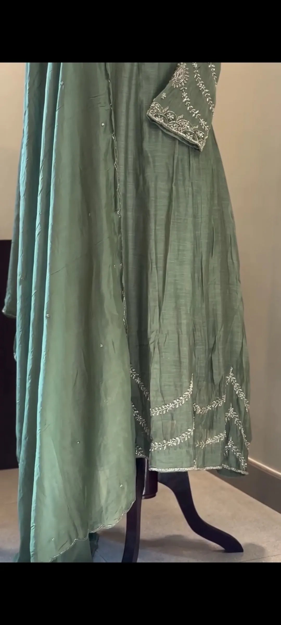Green dress with white embroidery on a mannequin against a neutral wall.