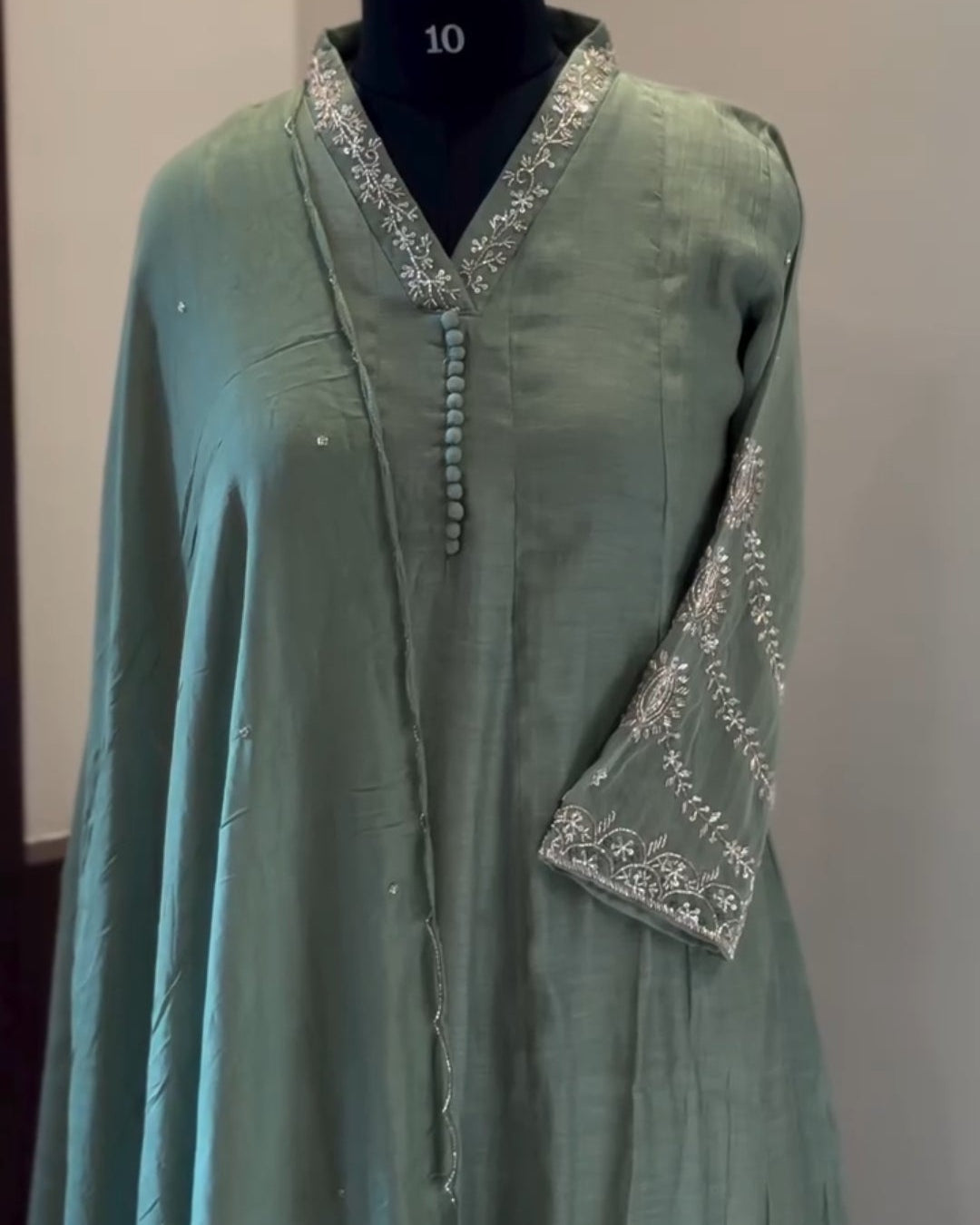 Green dress with silver embroidery on a mannequin against a plain background