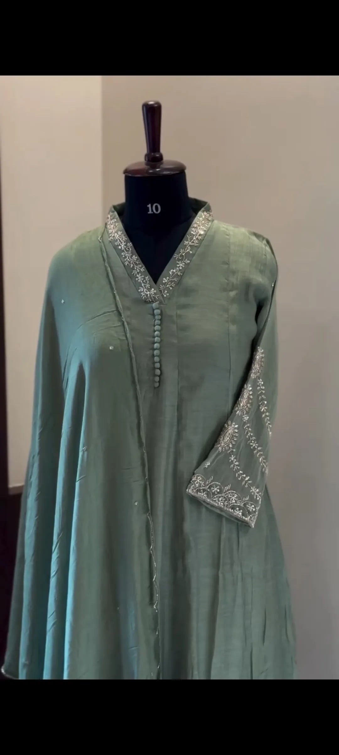 Green dress with silver embroidery on a mannequin against a plain background