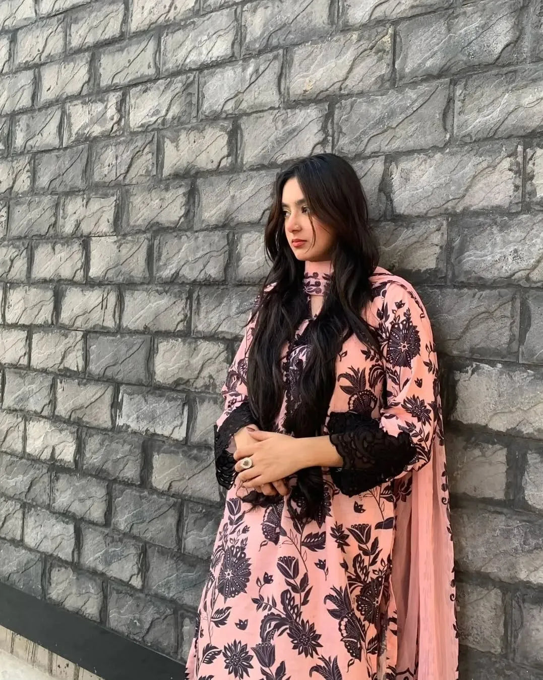 Woman wearing a pink floral dress against a stone wall