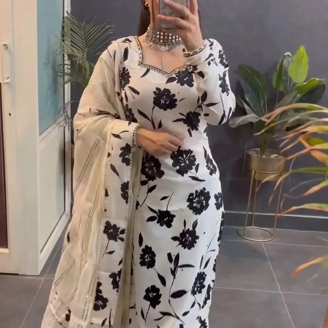 Person wearing a white outfit with black floral patterns in a room with plants.