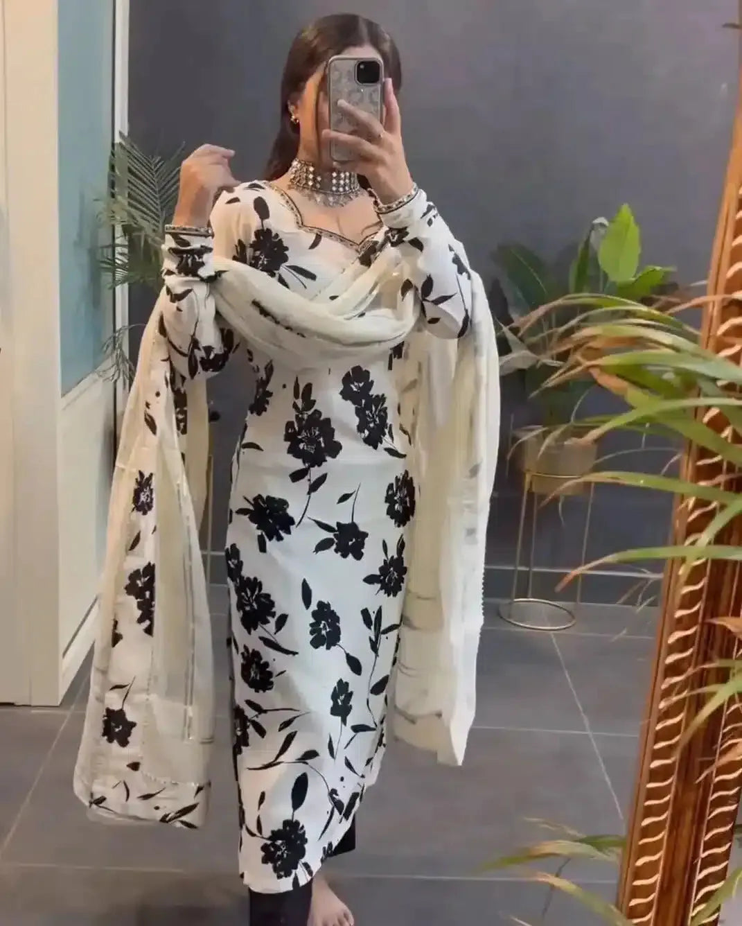 Person wearing a black and white floral outfit with a matching scarf indoors.