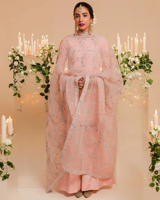 Woman in a pink traditional outfit standing in front of decorative candles and flowers.