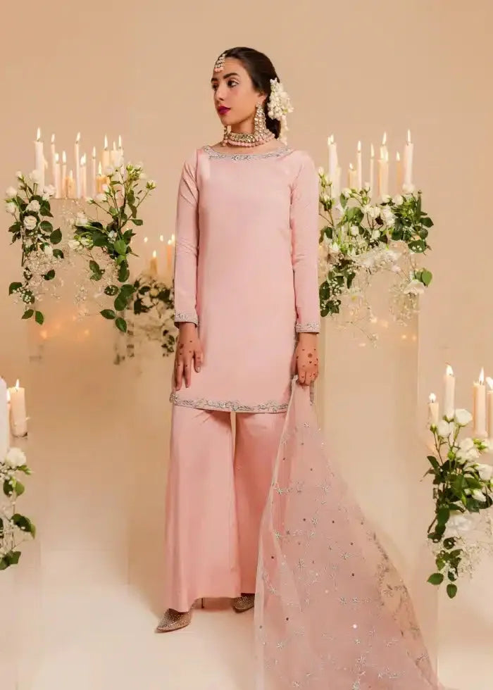 Woman in a pink traditional outfit standing in front of decorative candles and greenery.
