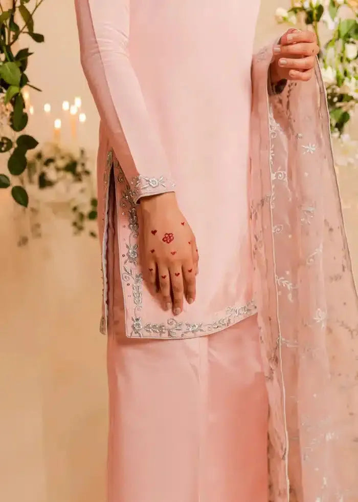 Person wearing a light pink traditional outfit with a floral design, holding a matching dupatta.
