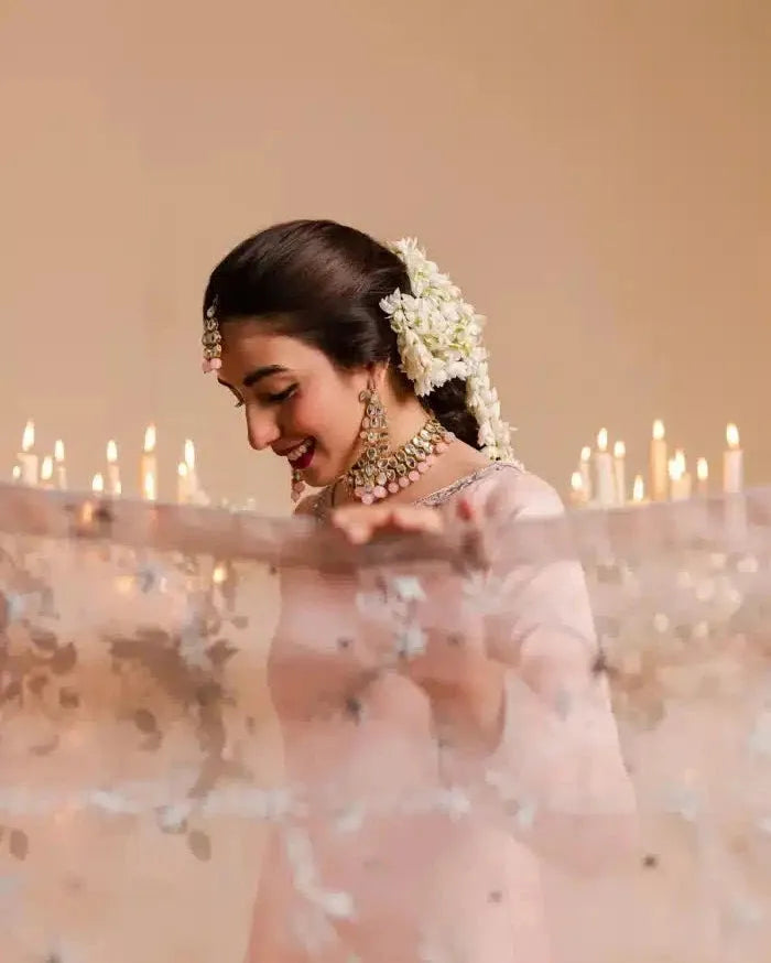 Woman in traditional attire with floral hairpiece and jewelry, candles in the background