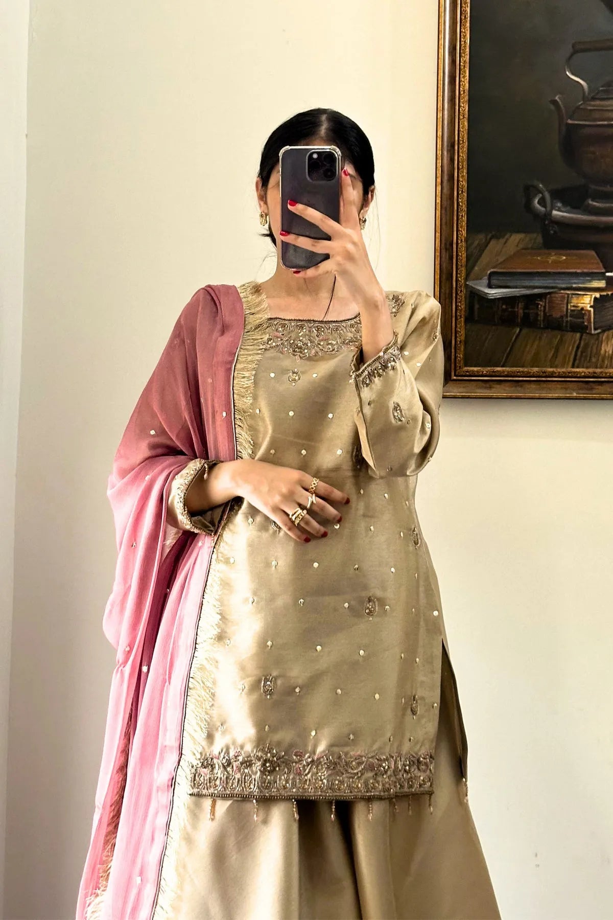 Person wearing a gold embroidered outfit with a pink dupatta, taking a mirror selfie.