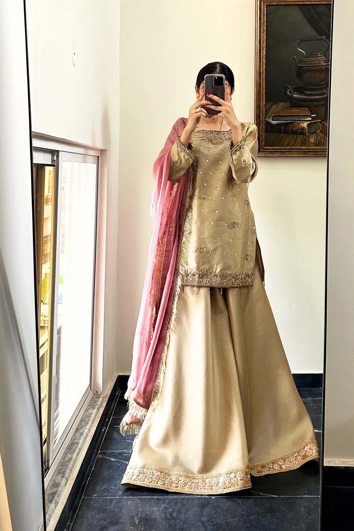 Person wearing a traditional outfit with a pink dupatta in front of a mirror.