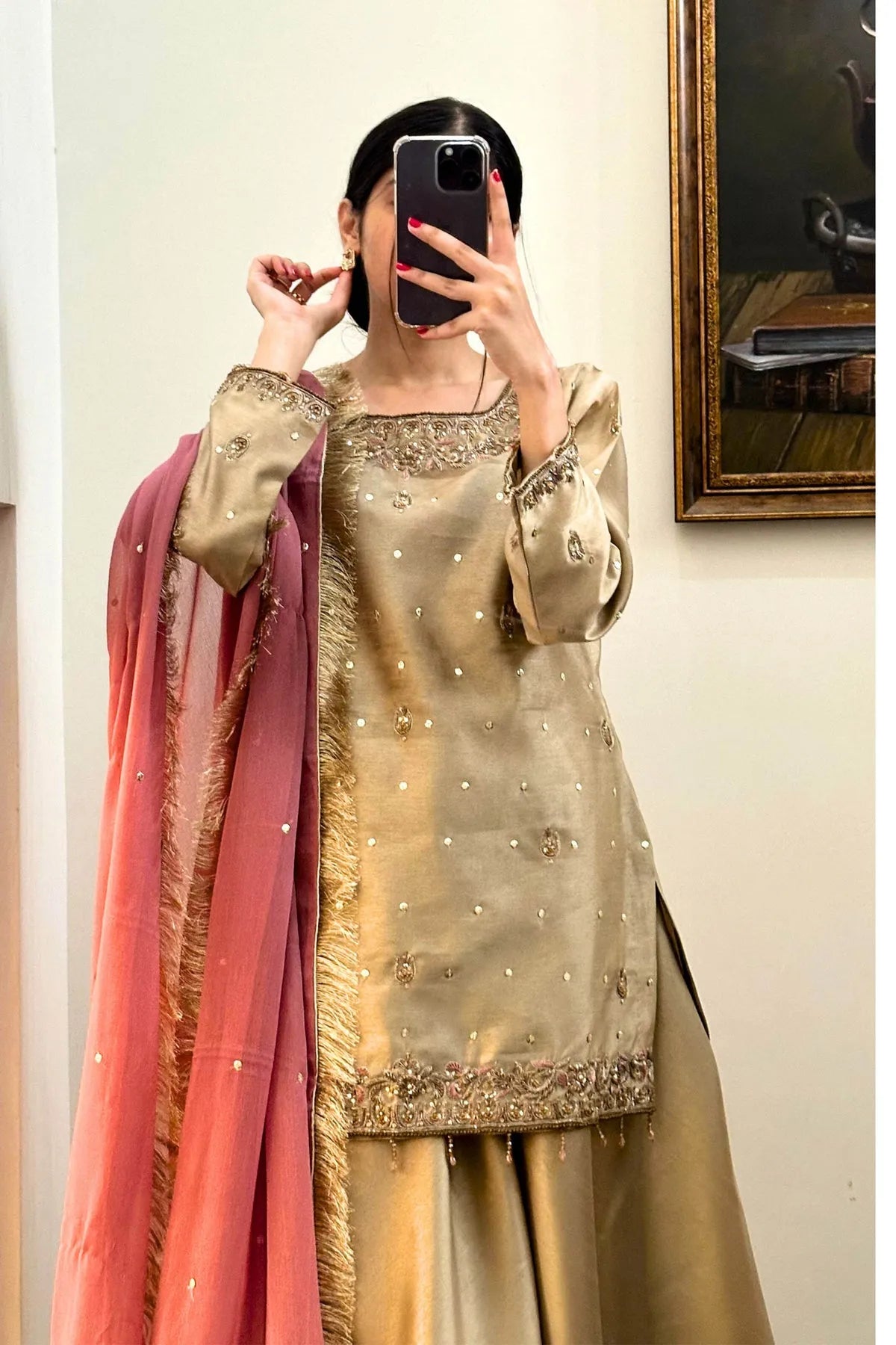 Person wearing a traditional outfit with a gold and pink dupatta taking a mirror selfie.
