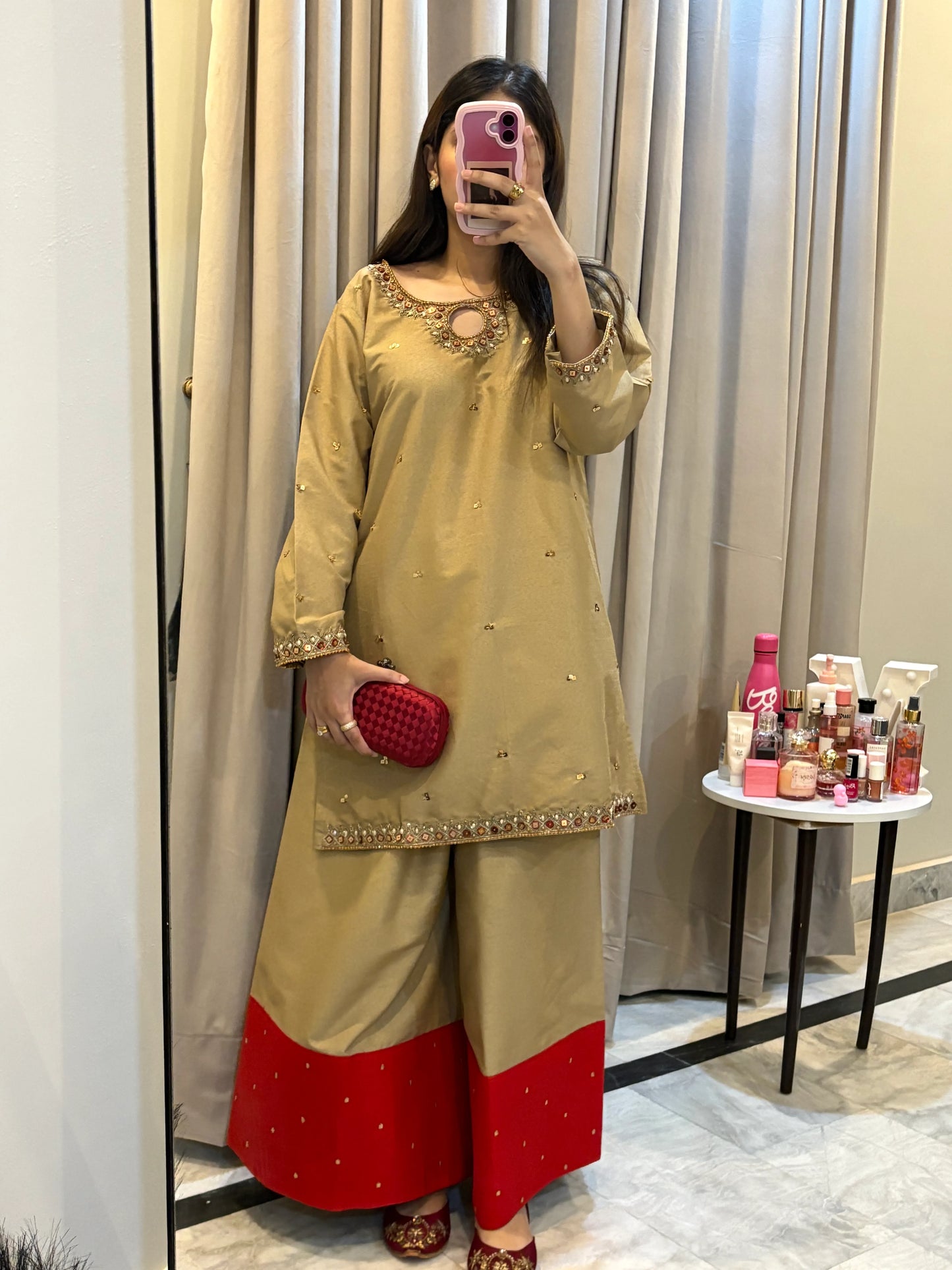 Woman taking a mirror selfie wearing a traditional outfit with green and red details.