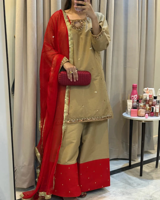 Person wearing a beige and red traditional outfit with a red clutch, standing in front of a mirror.