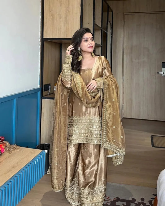 Woman in a gold traditional outfit standing indoors.