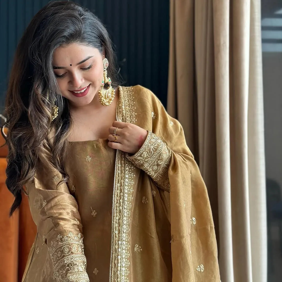 Woman in a traditional outfit with gold and beige colors, standing indoors.