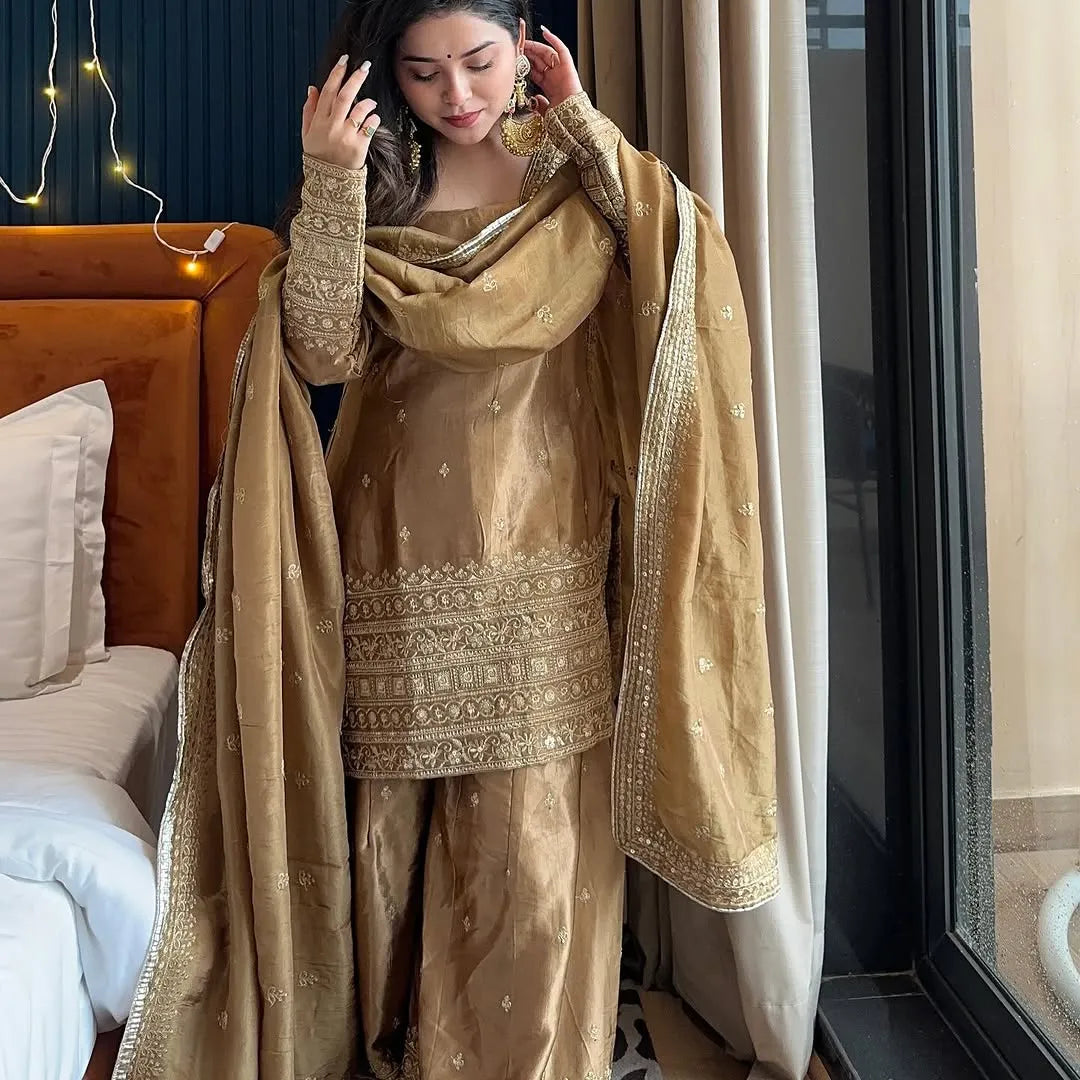 Woman in a beige embroidered traditional outfit standing in a bedroom.