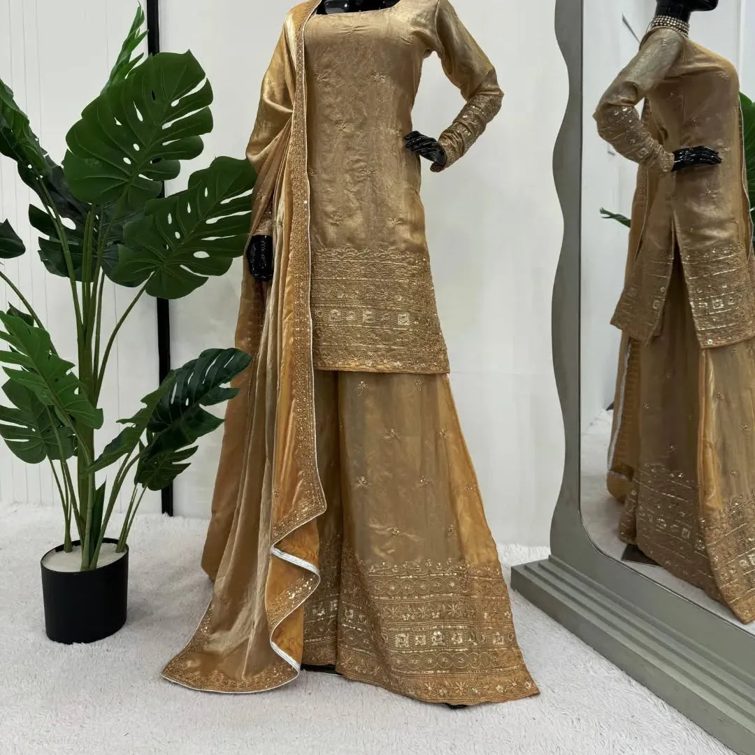 Gold embroidered traditional outfit displayed on a mannequin with a plant in the background.