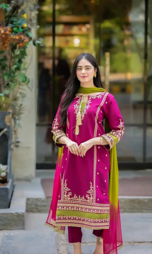 Woman wearing a pink and green traditional outfit with intricate patterns, standing outdoors.