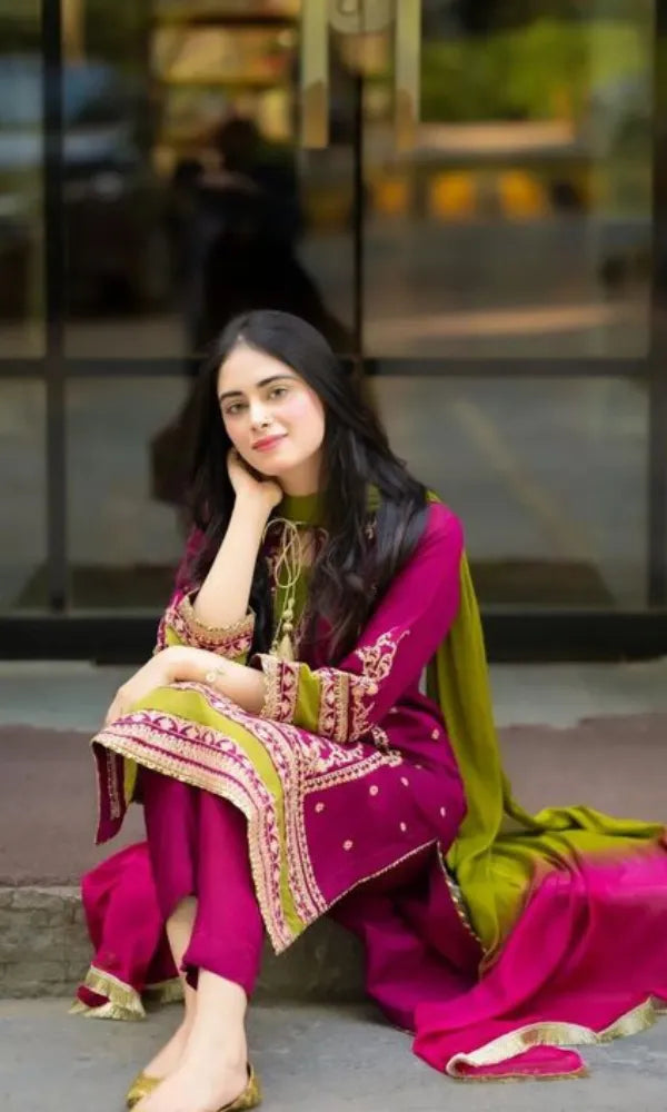 Woman in a pink and green traditional outfit sitting outdoors.