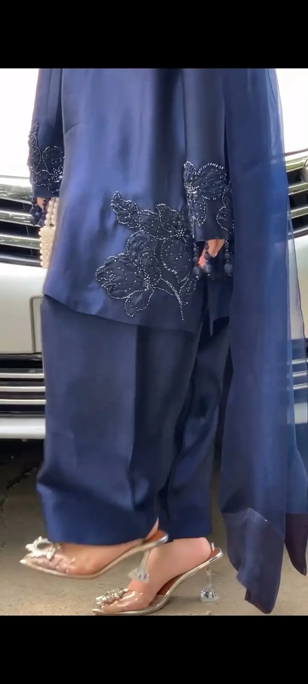 Person wearing a blue outfit with floral embroidery in front of a car.