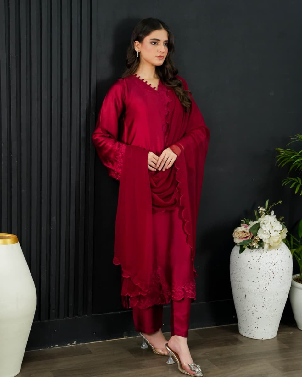 Woman in a red outfit standing against a black wall with decorative vases and plants.