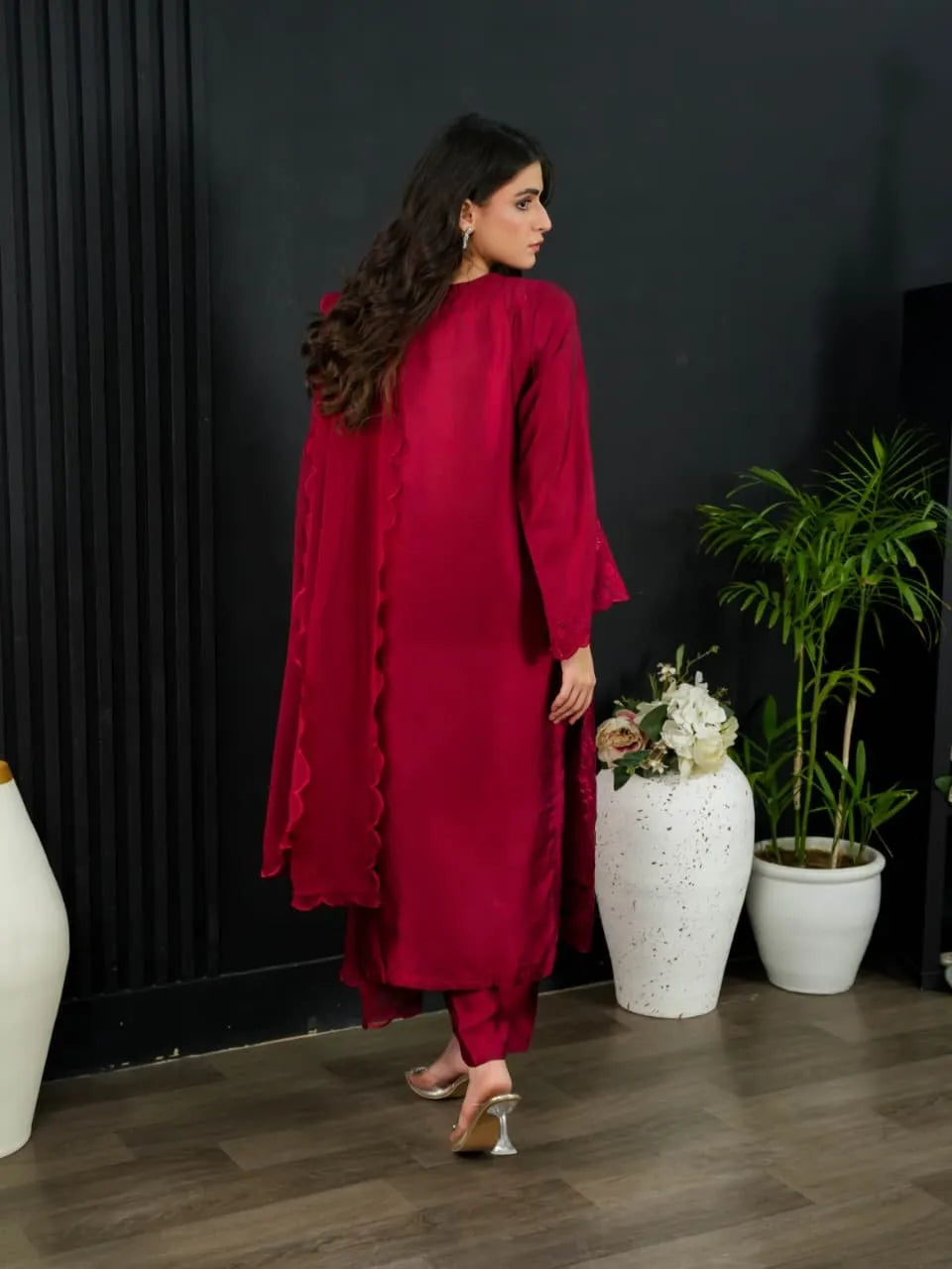 Woman in a red outfit standing in a room with decorative plants and vases.