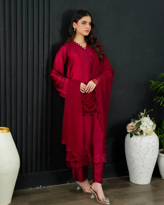 Woman in a red traditional outfit standing against a dark wall with decorative vases and plants.