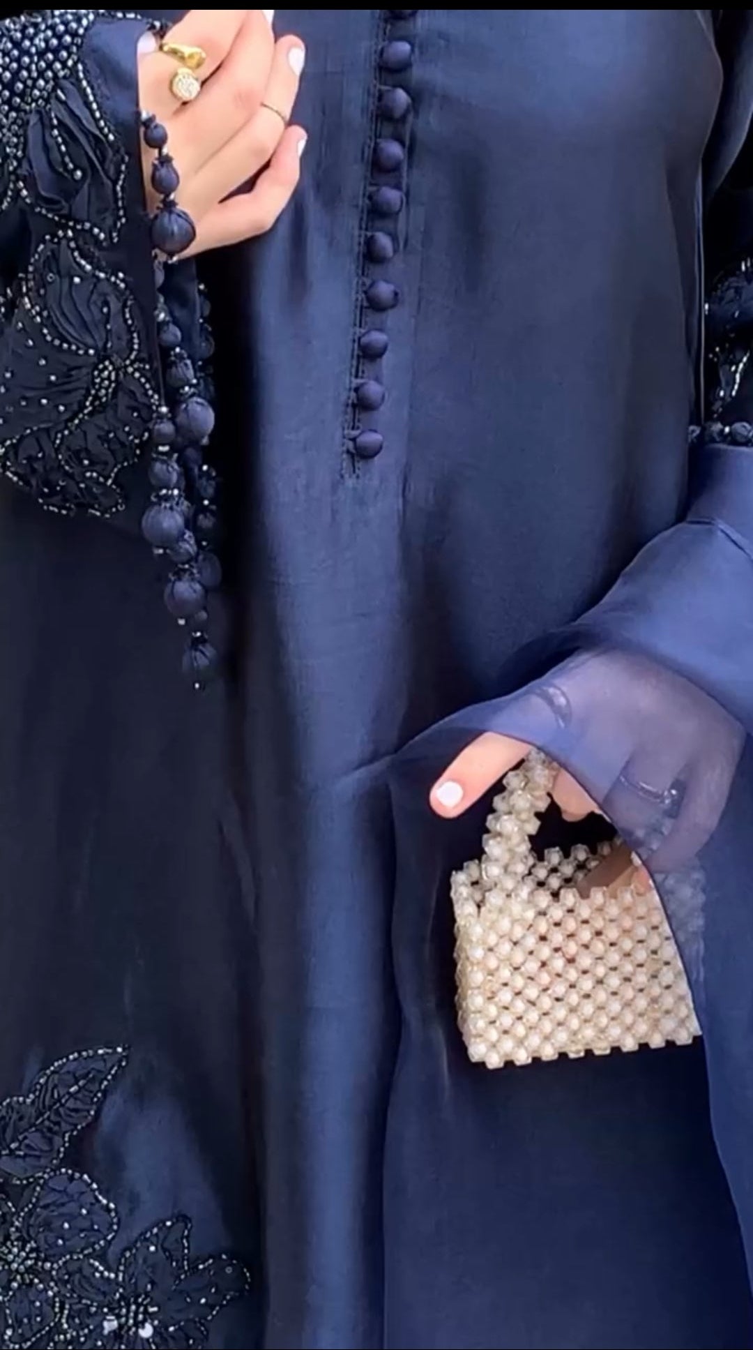 Person wearing a dark blue outfit with a beaded handbag